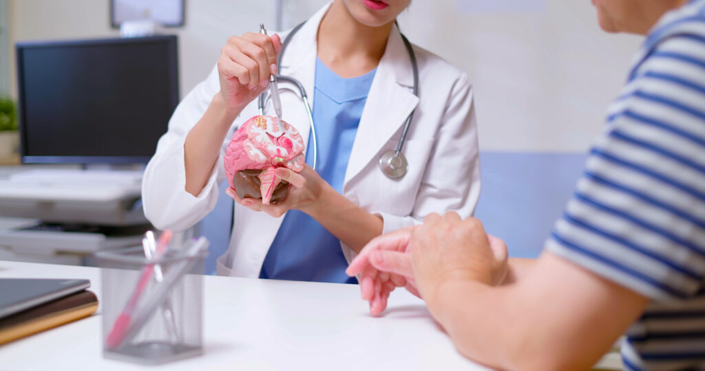closeup of doctor wear white coat and stethoscope pen pointing explaining brain model to man at clinic, brain injury theme