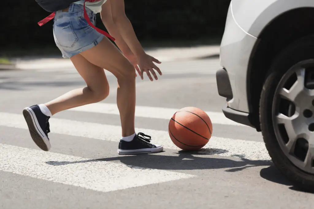 Young girl catching a basket ball on a pedestrian crossing, pedestrian accident theme