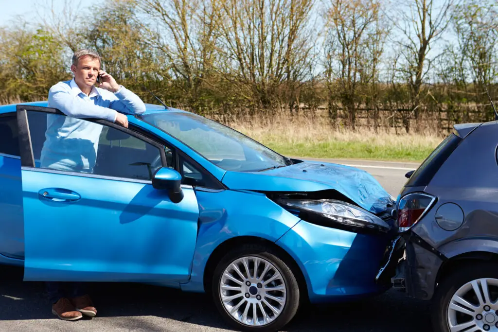 A driver making a phone call after a rear-end accident that damaged both vehicles and led to possible whiplash injuries. 