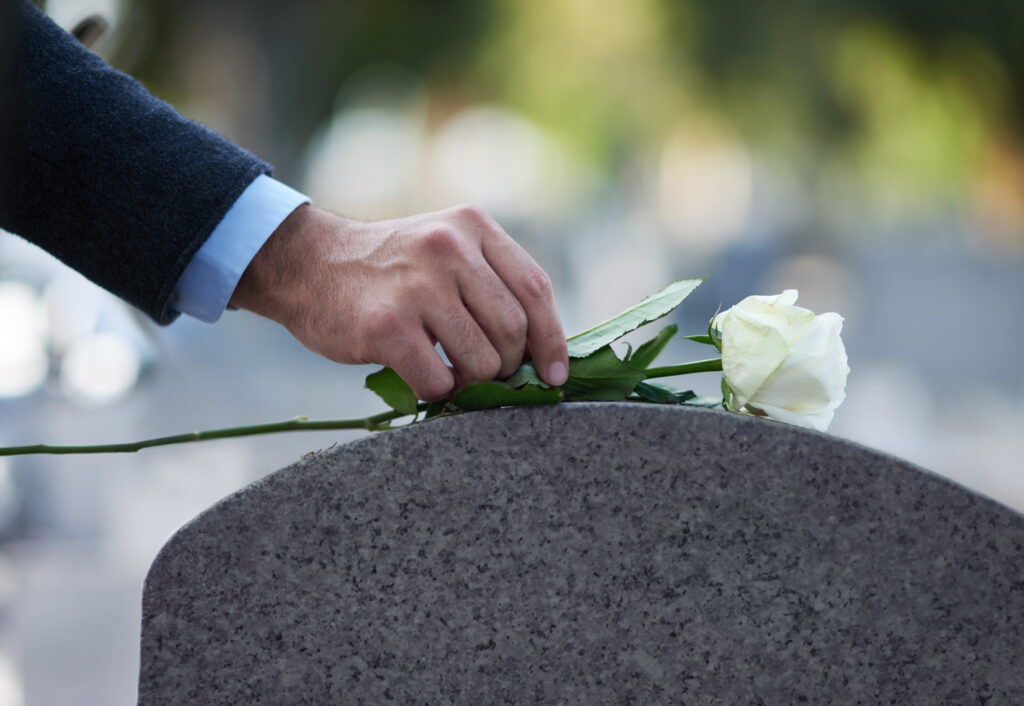 Cropped shot of a man placing a white rose on a grave, wrongful death concept