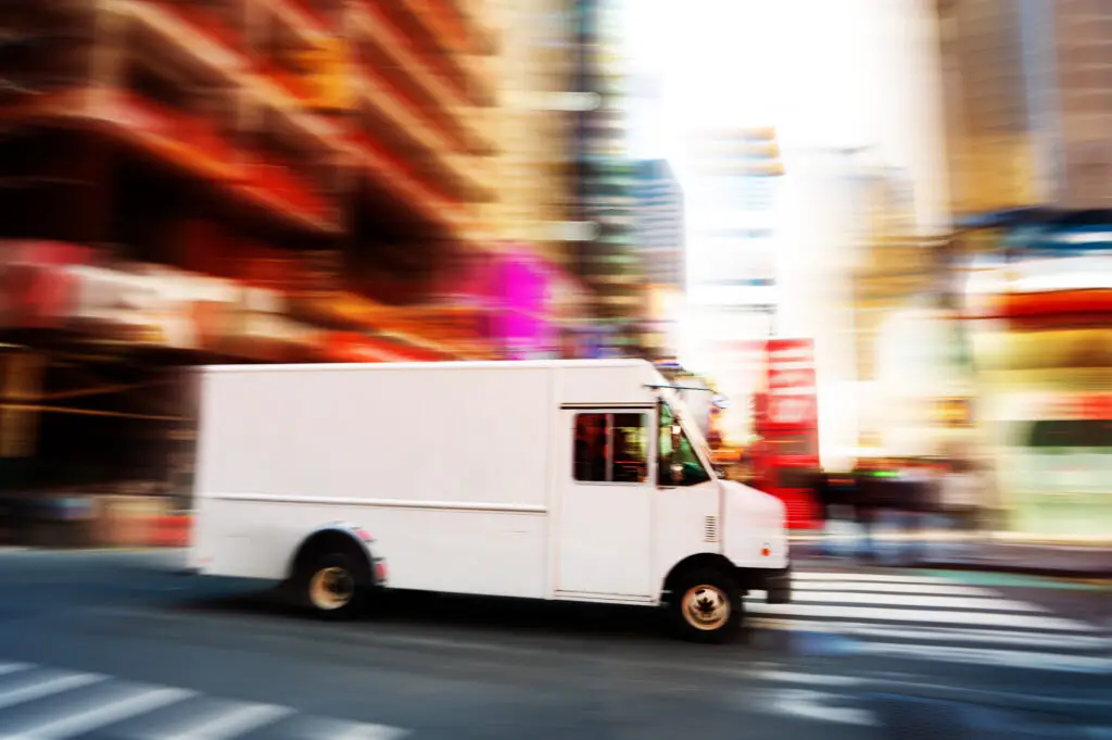 White delivery truck speeding down an urban street, with a blurred background.