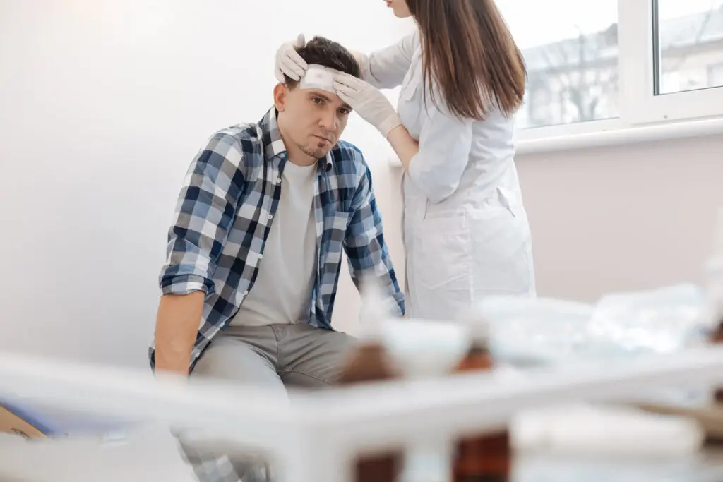 man sitting on the medical bed and receiving the first aid for his head injury after a personal injury accident