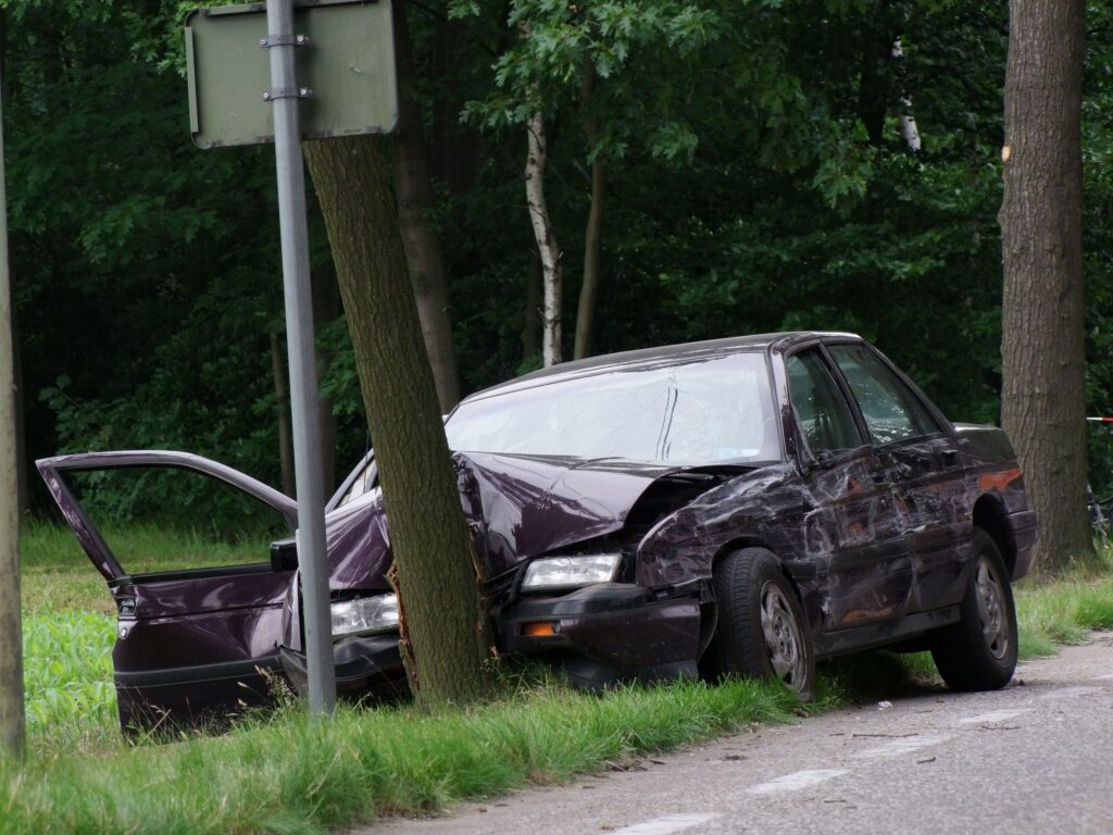 a burgundy colored car that has smashed its front end into a tree off the side of a road