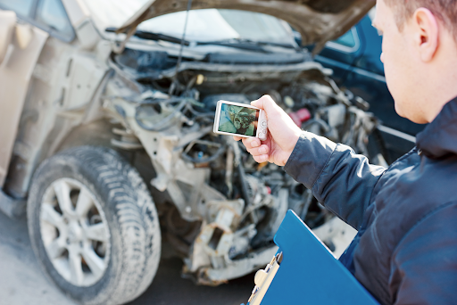 An insurance adjuster takes a photograph of an automobile with significant front end damage from an accident.