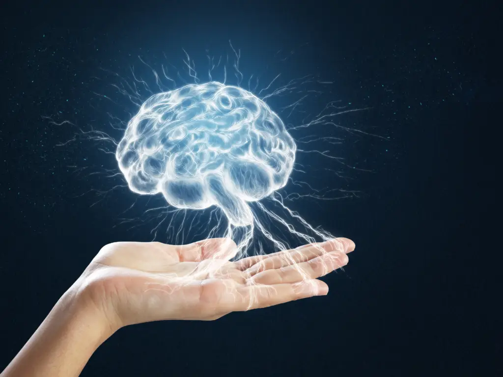 hand holding an illuminated brain with neurons coming from it