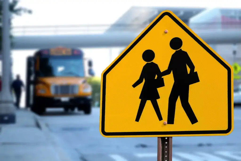 traffic sign to watch for pedestrians on a road way, pedestrian stepping onto a bus in the background