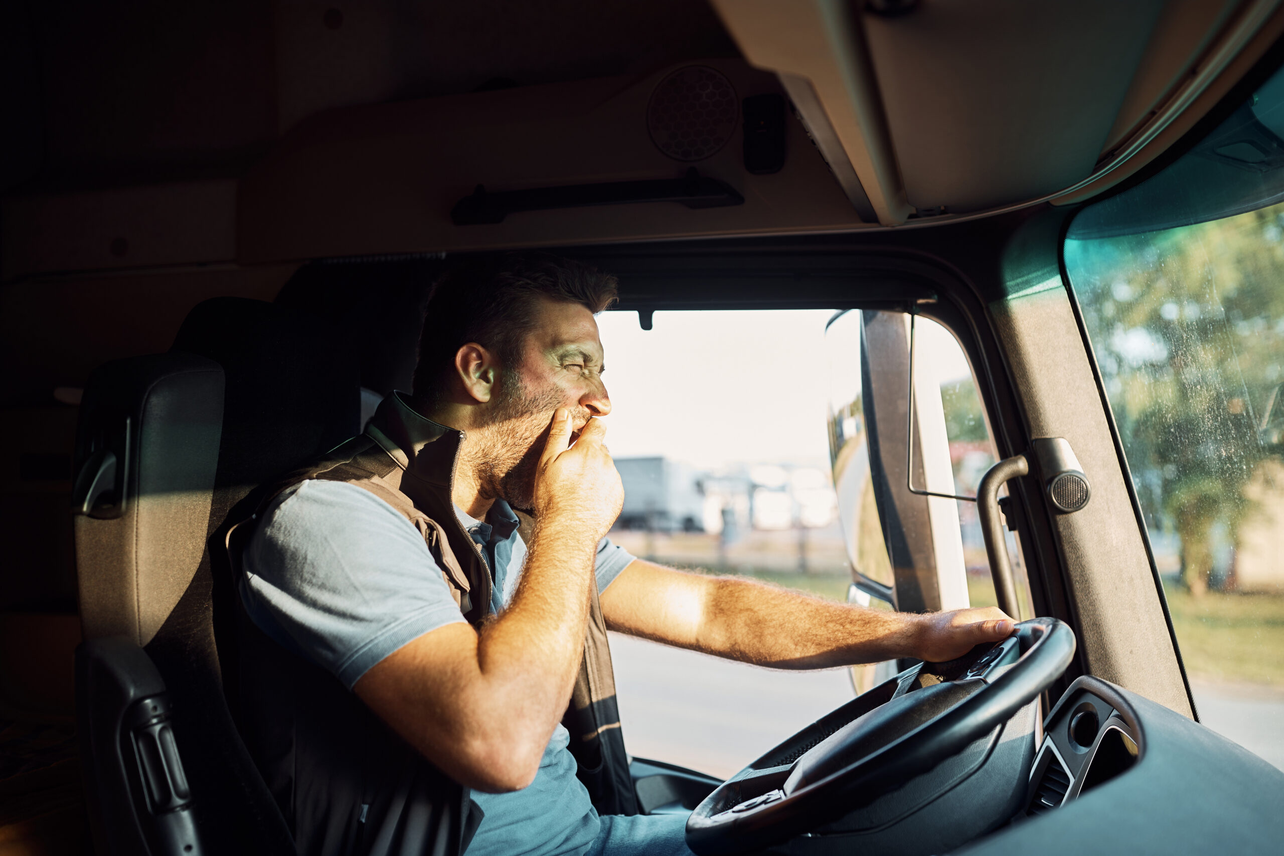 A truck driver yawns while behind the wheel of his semi-truck. 