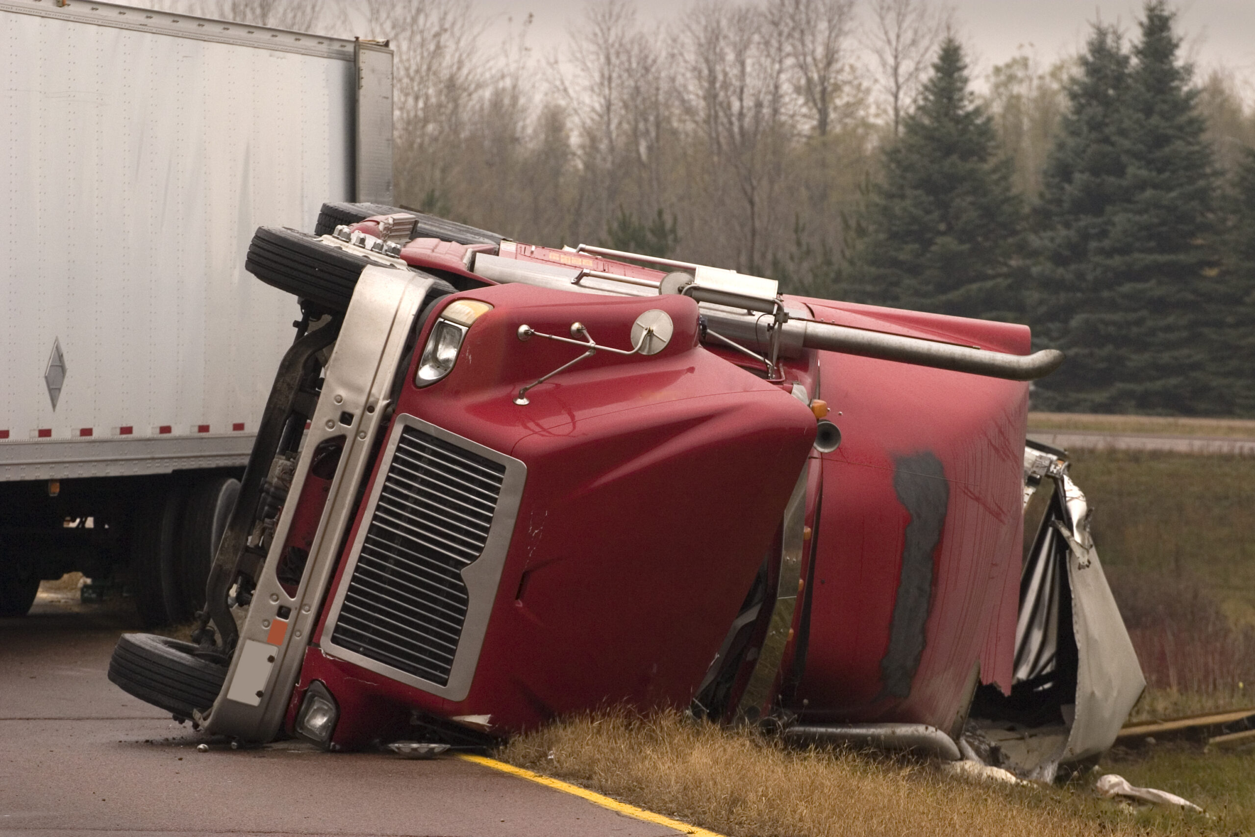 A jackknife truck accident that has cause the cab of the truck to overturn, causing heavy damage to the semi cab.