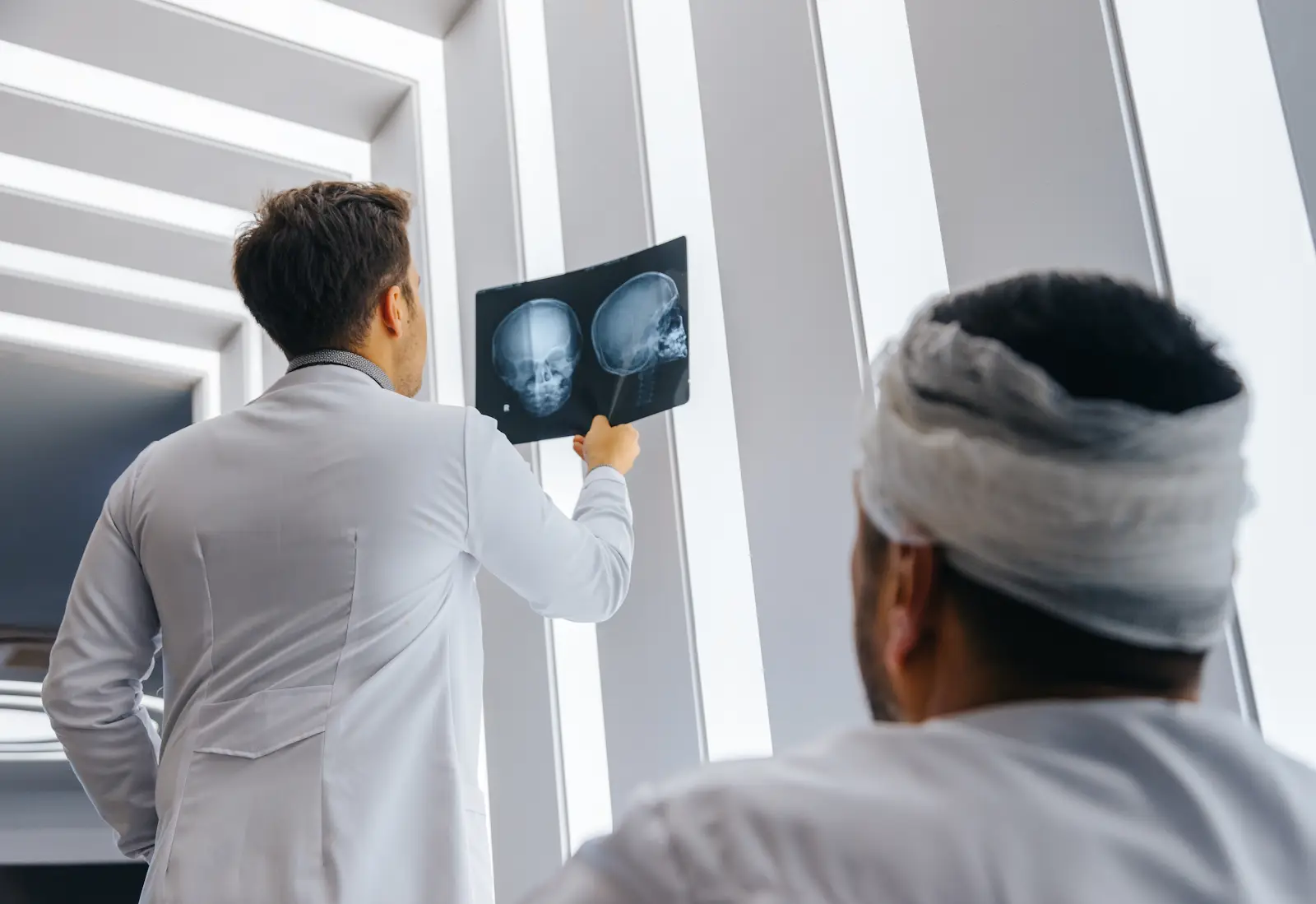 Man with whiplash looking at his doctor, who is showing him his xrays of his skull, neck, and spinal cord.