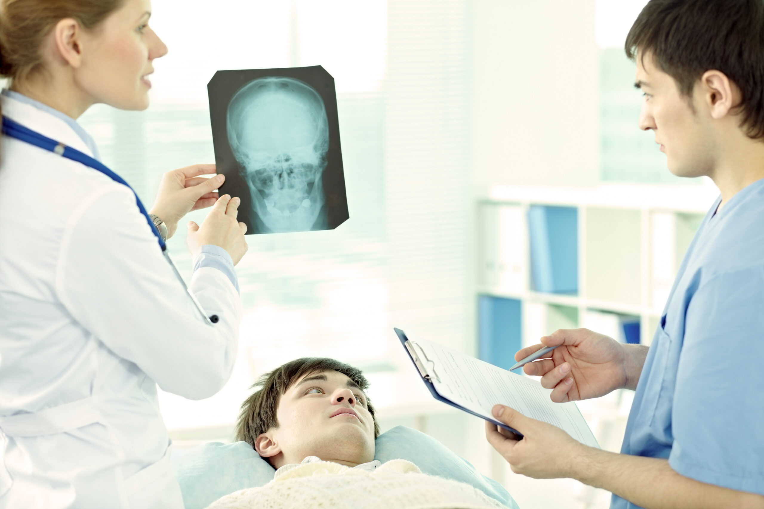 Young man lying in hospital with head injury, doctor examining his brain x-ray