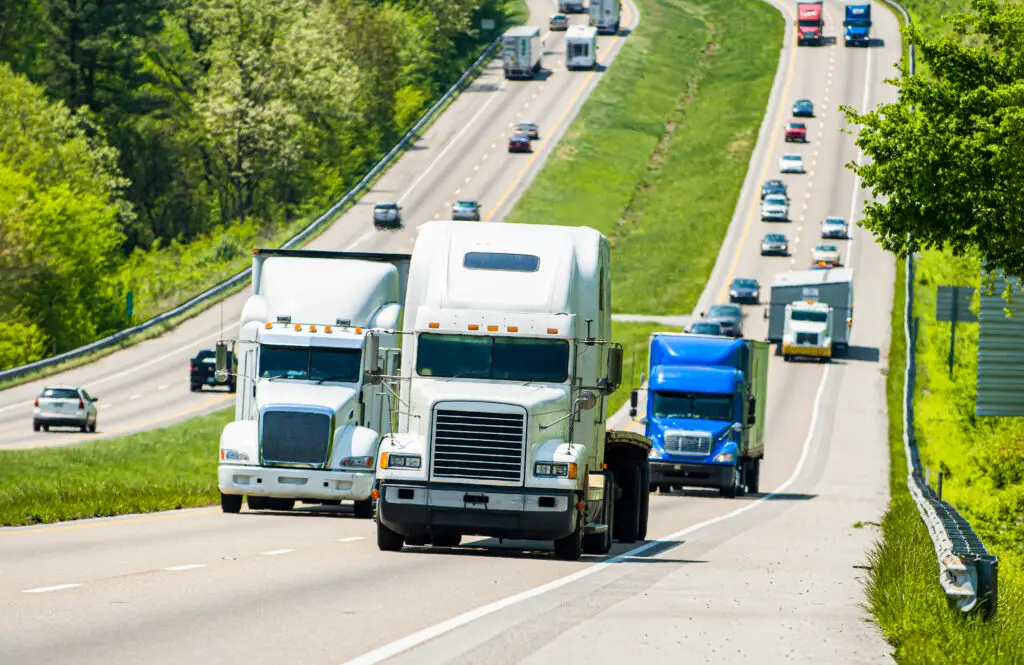 A semi cab that is "bobtailing" drives up a hill on a busy highway.