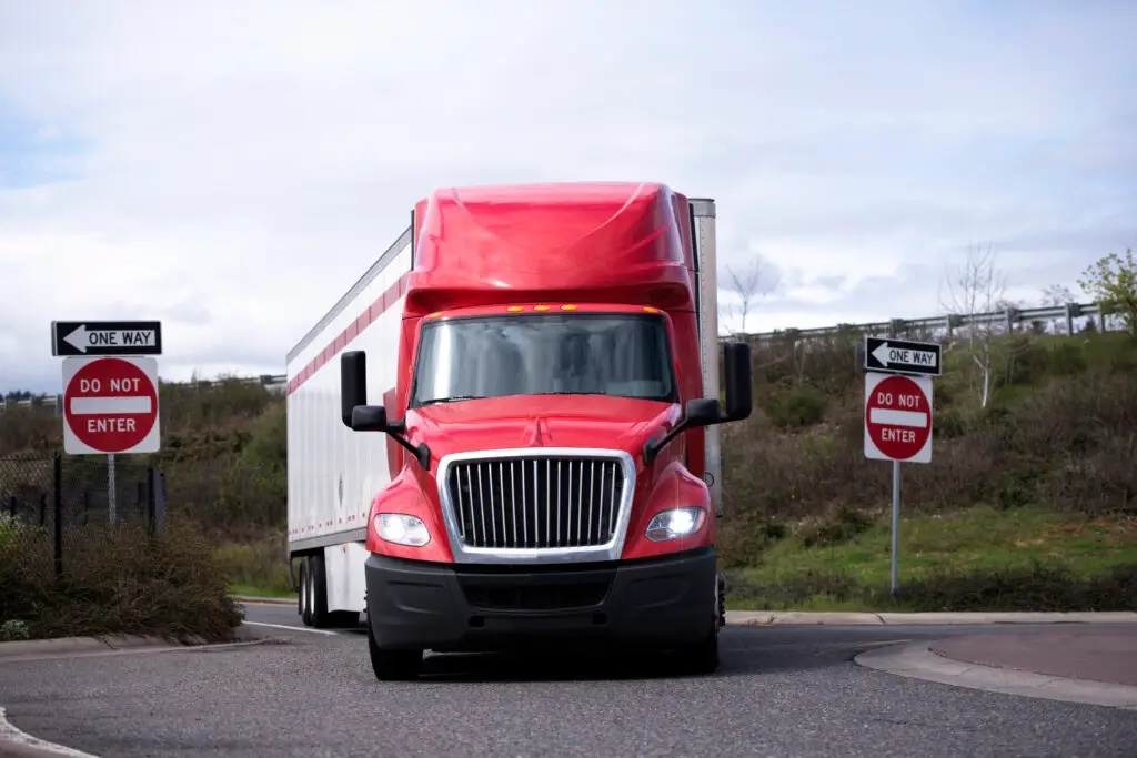 A red and white semi truck takes a turn off an exit ramp from the highway.