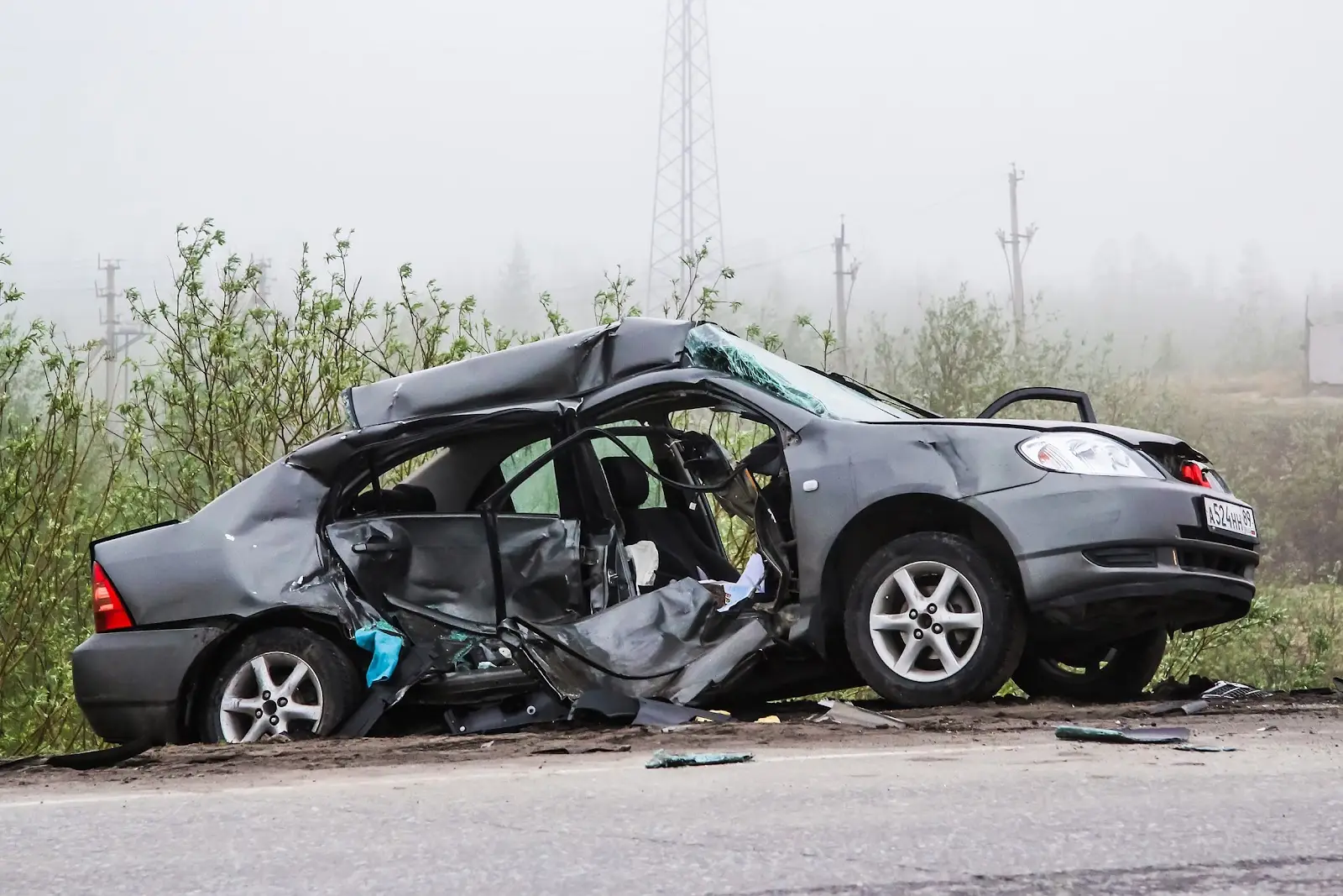 A damaged, grey sedan sits in a ditch on the side of the road after a deadly car accident
