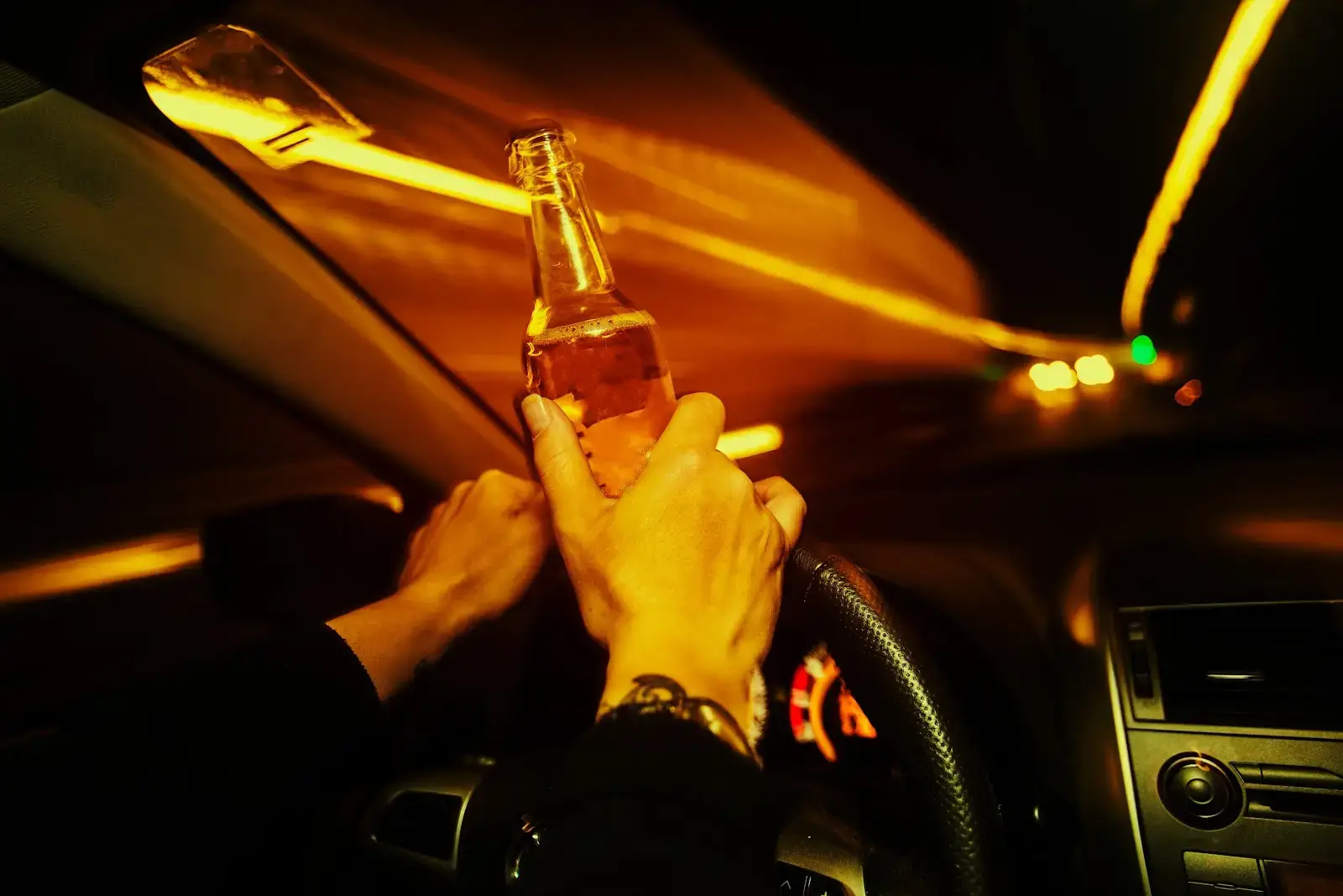 An image of a person operating a motor vehicle with a beer and cigarette in their hand