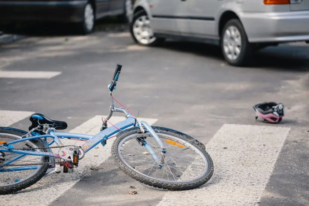A damaged blue bicycle and bicycle helmet on the ground in the middle of a crosswalk after an accident caused by a distracted driver. 