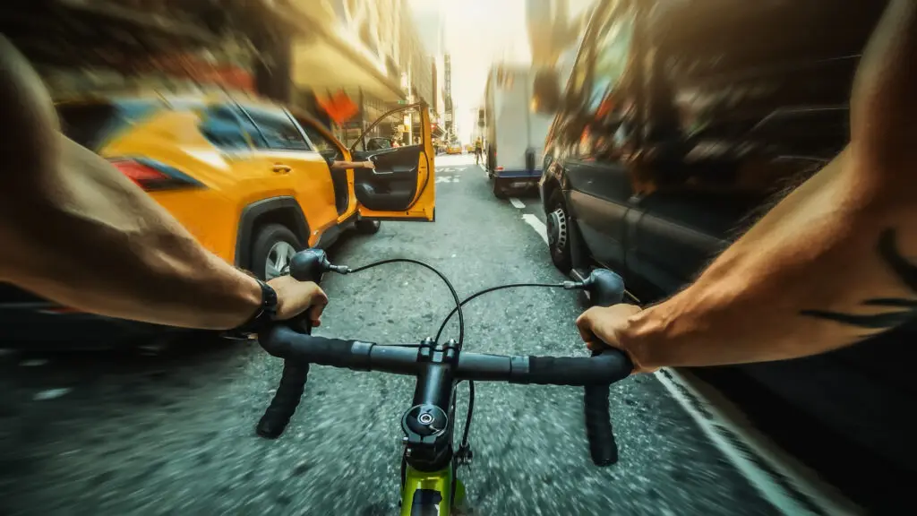 A passenger exits a taxi cab and opens the door into the path of a bicyclist, causing a dooring accident. 